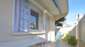 En terrasse med et hvidt bord og stole, et vindue med blomstret gardin og udsigt over det omkringliggende område.