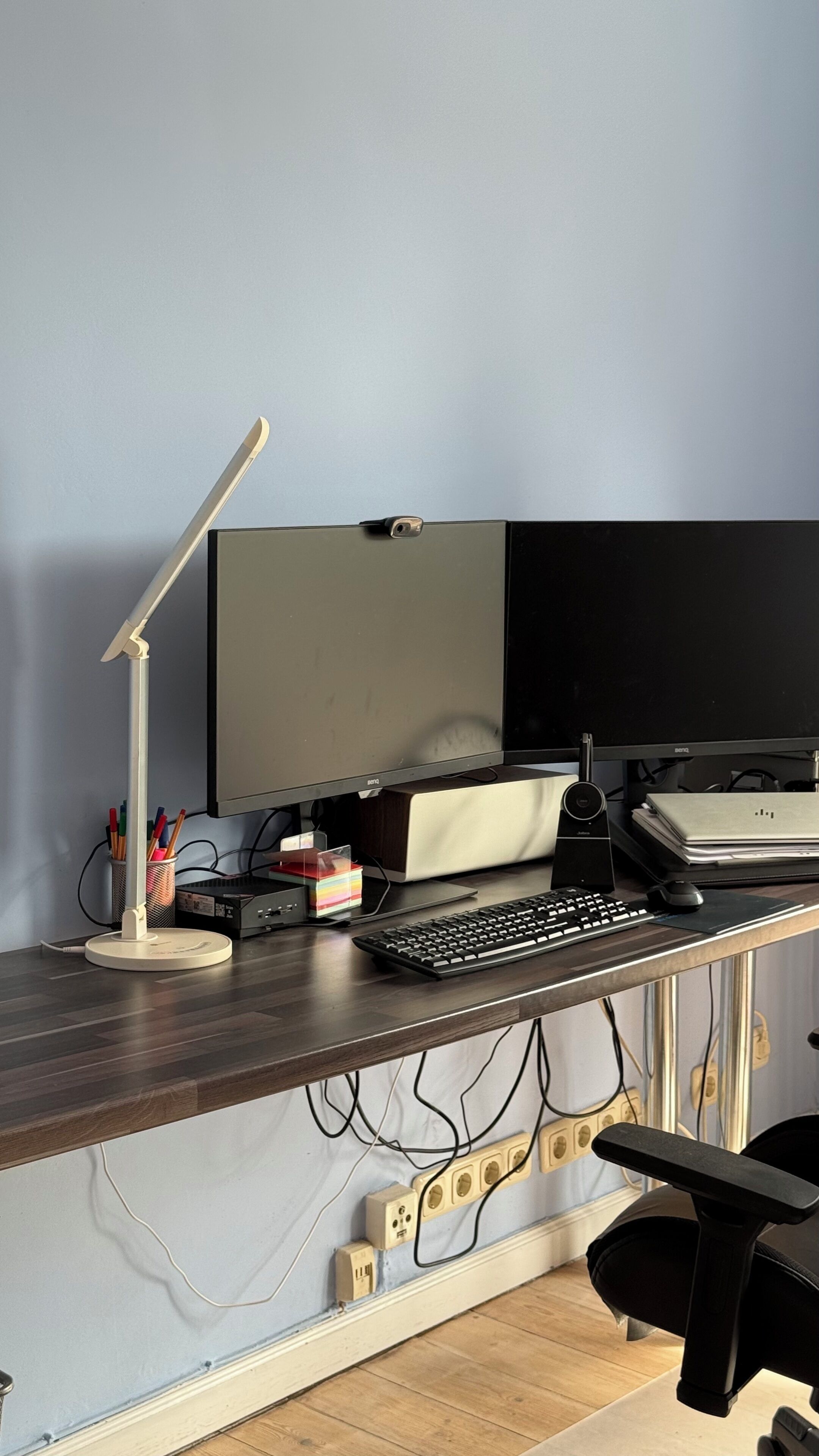 A desk with a computer, keyboard, mouse, and monitor. There are cables, a lamp, and a sticky note on the desk.