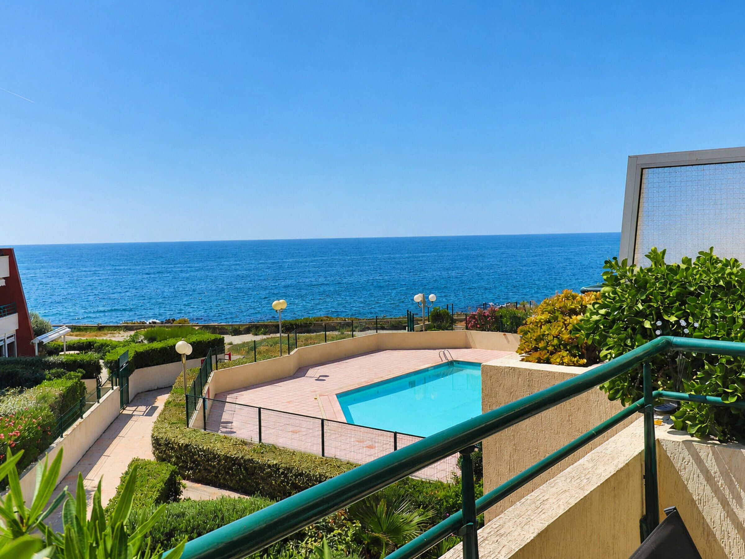 Une piscine avec vue sur la mer, entourée de verdure et un bâtiment doté d’un balcon.