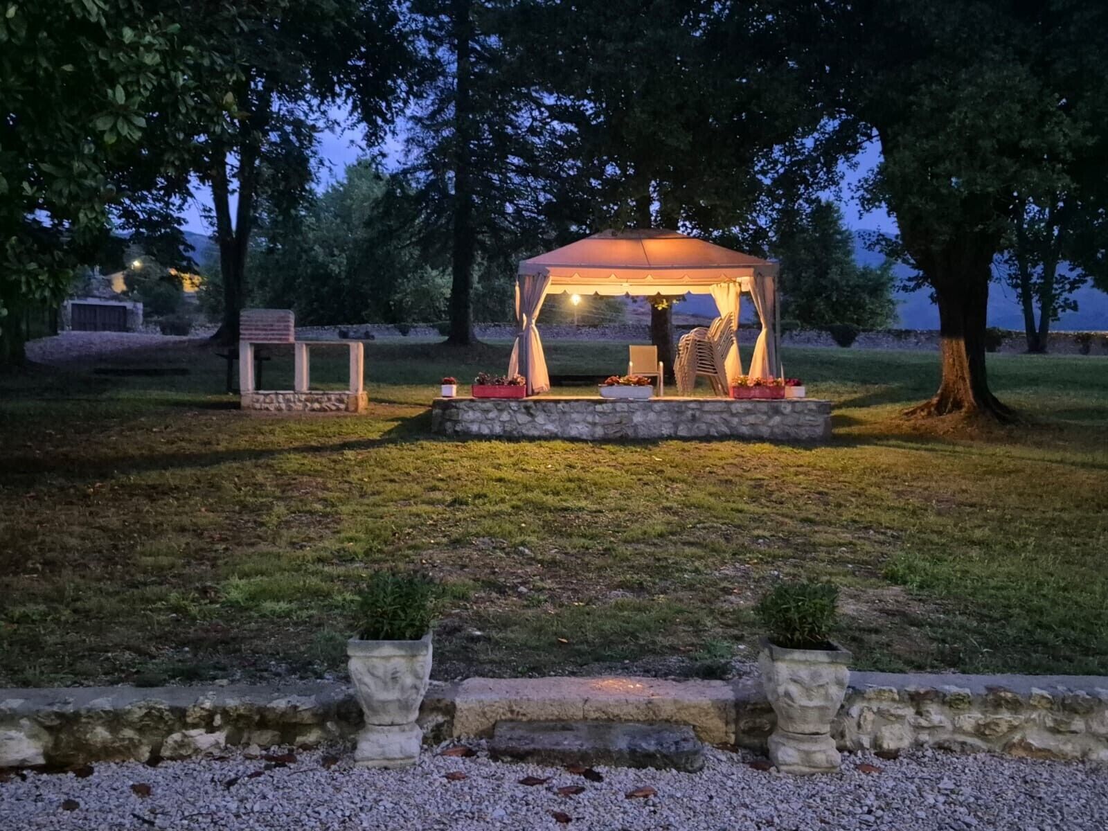 A gazebo with a stone base, surrounded by grass and trees.