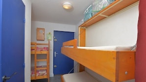 Een kamer met stapelbedden, een deur, een klein bureau en een wandplank.