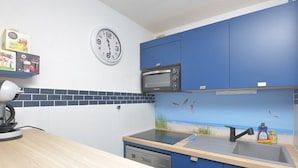 Een keuken met een klok, magnetron en blauwe kastjes.