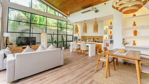 Una sala de estar moderna con sofá, mesa de comedor, sillas, televisor y una zona de cocina con barra.