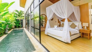 Un dormitorio con una cama grande, dosel, mesita de noche y vistas a una piscina.