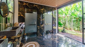 Un baño moderno con tocador de mármol, un espejo grande y vistas a un jardín tropical.