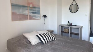 Ein Schlafzimmer mit einem Bett, einer Nachttischlampe, einem kleinen Tisch mit Spiegel und einem Wandbild.