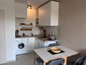Una kitchenette compacta equipada con lavadora, microondas, tostadora y un pequeño comedor con mesa y sillas.