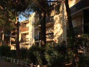 Un edificio residencial de varios pisos con balcones, rodeado de árboles y arbustos.