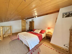 A bedroom with a wooden ceiling, a bed with red and white bedding, a nightstand with a lamp, and a wooden wardrobe. - Apartment pets allowed - 8 guests (Praz-sur-Arly)