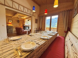 A dining area with a long table set for four, a fireplace, and a view of the mountains. - Apartment pets allowed - 8 guests (Praz-sur-Arly)