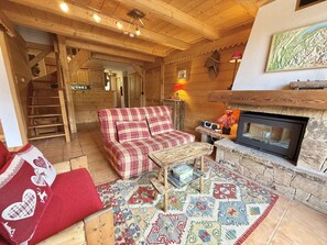 A cozy room with a checkered sofa, a small table, a fireplace, and a staircase leading to another area. - Apartment pets allowed - 8 guests (Praz-sur-Arly)