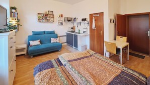 Un espacio habitable compacto con kitchenette, un sofá, una cama con colcha estampada y un escritorio.