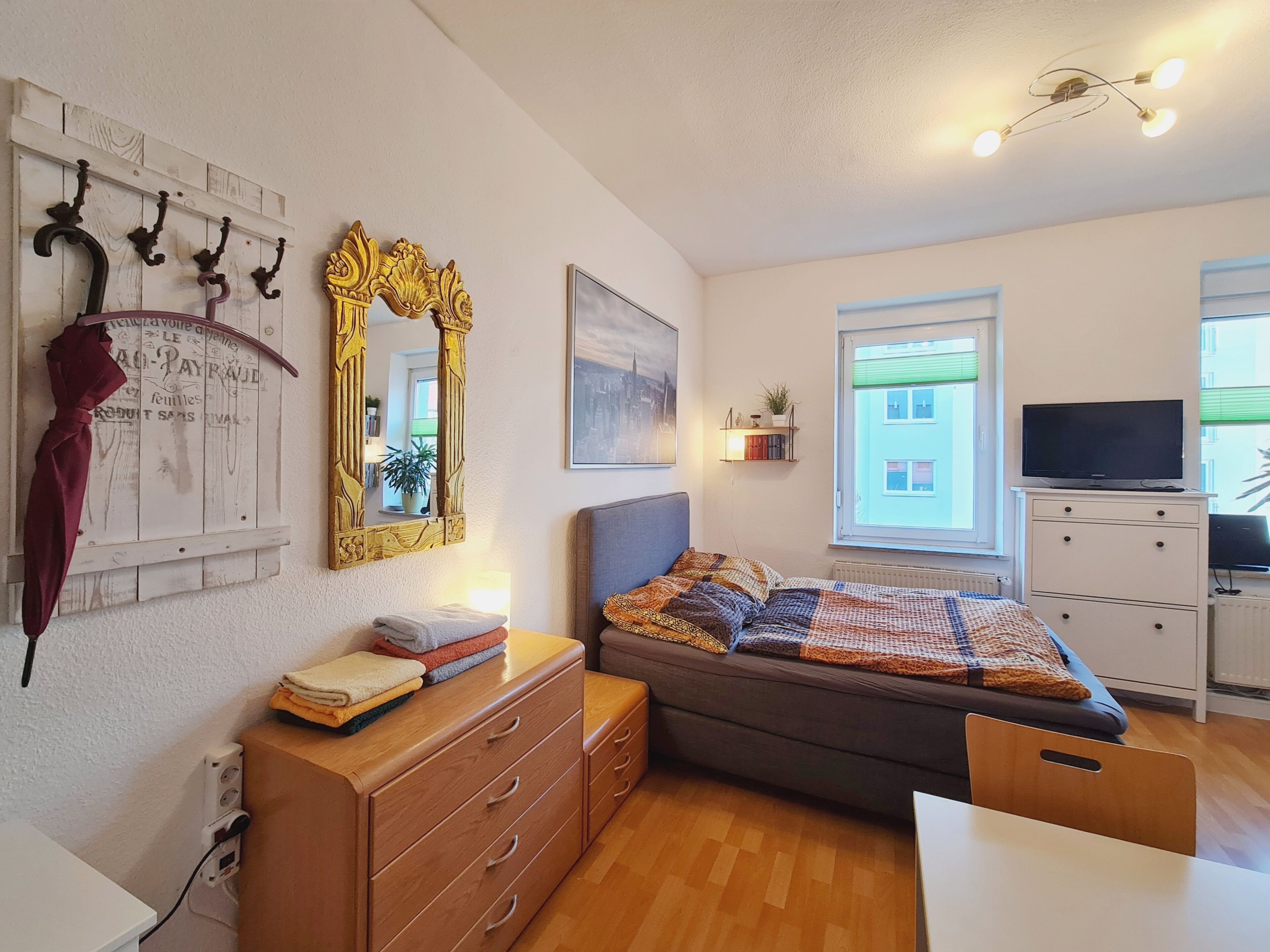A bedroom with a bed, dresser, TV, and a window with a view.