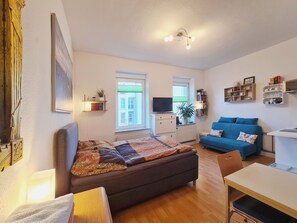 A cozy room with a bed, a blue sofa, a small table, and a TV. - Apartment by the Park (Erfurt)