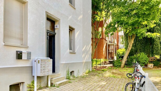 Un edificio con fachada blanca, un cartel con el número 16, una bicicleta estacionada afuera y un patio empedrado.
