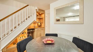 A dining area with a round table, chairs, a decorative flower centerpiece, a staircase, and a mirror on the wall.