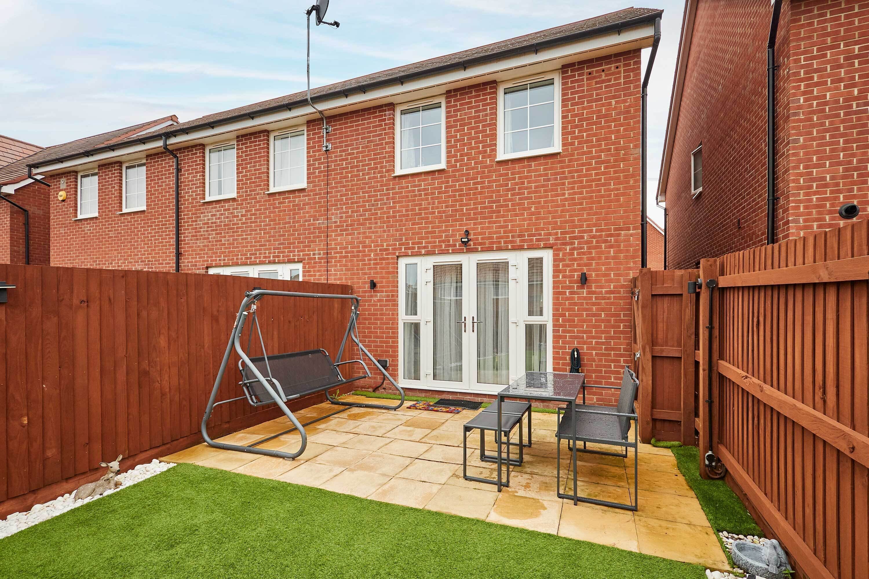 A residential backyard with a patio, a swing set, and a wooden fence.