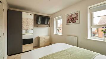 A bedroom with a bed, a dresser, a television, a window with a view, and a door.