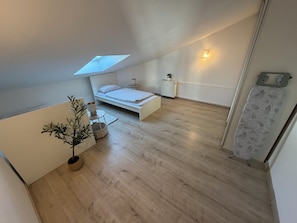 Ein kleines, modernes Schlafzimmer mit Oberlicht, einem Bett, einem Nachttischchen, einer Topfpflanze und einem Heizkörper.
