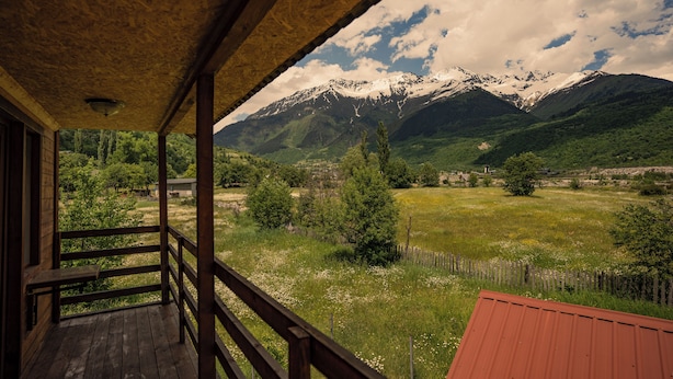Ein Holzbalkon mit Blick auf schneebedeckte Berge und ein grünes Feld.