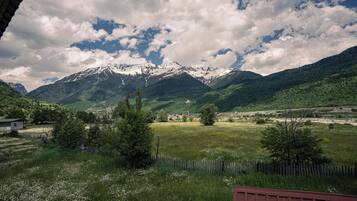 A mountainous landscape with snow-capped peaks, a grassy field, and a wooden fence.