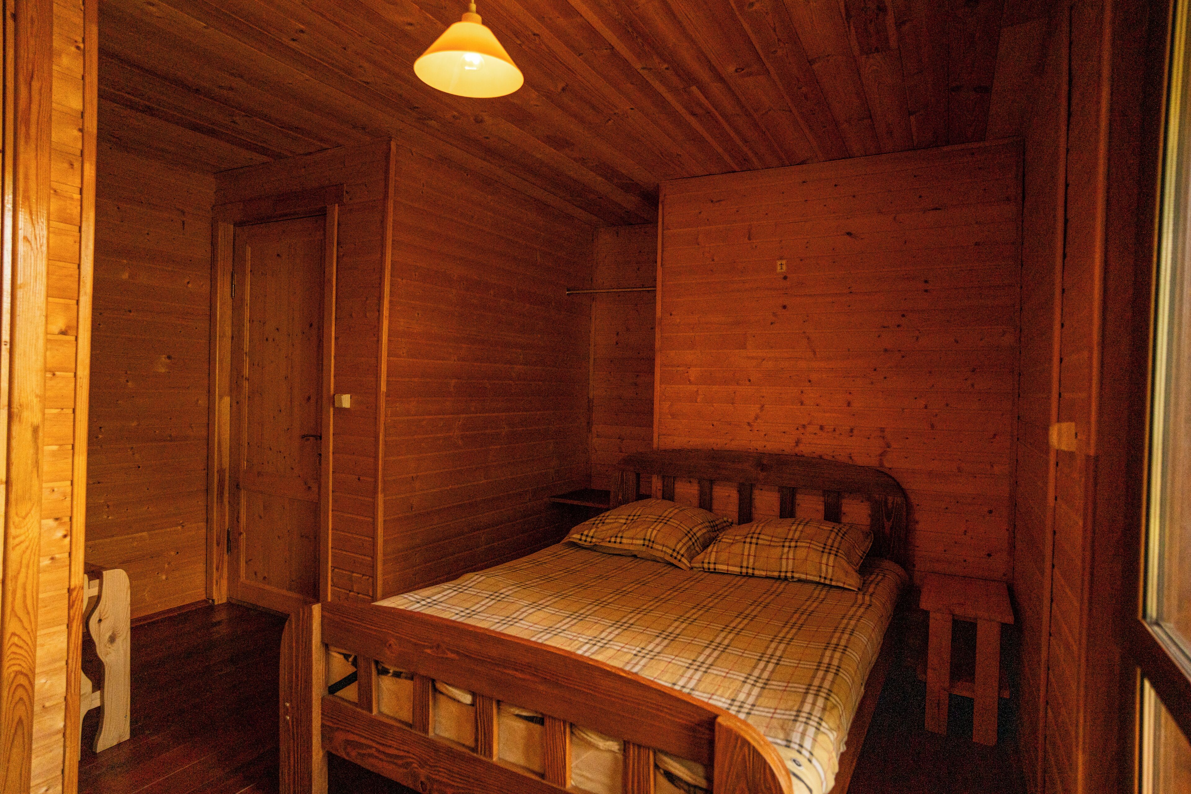 Una habitación de cabaña de madera con una cama, una mesita de noche y una ventana.