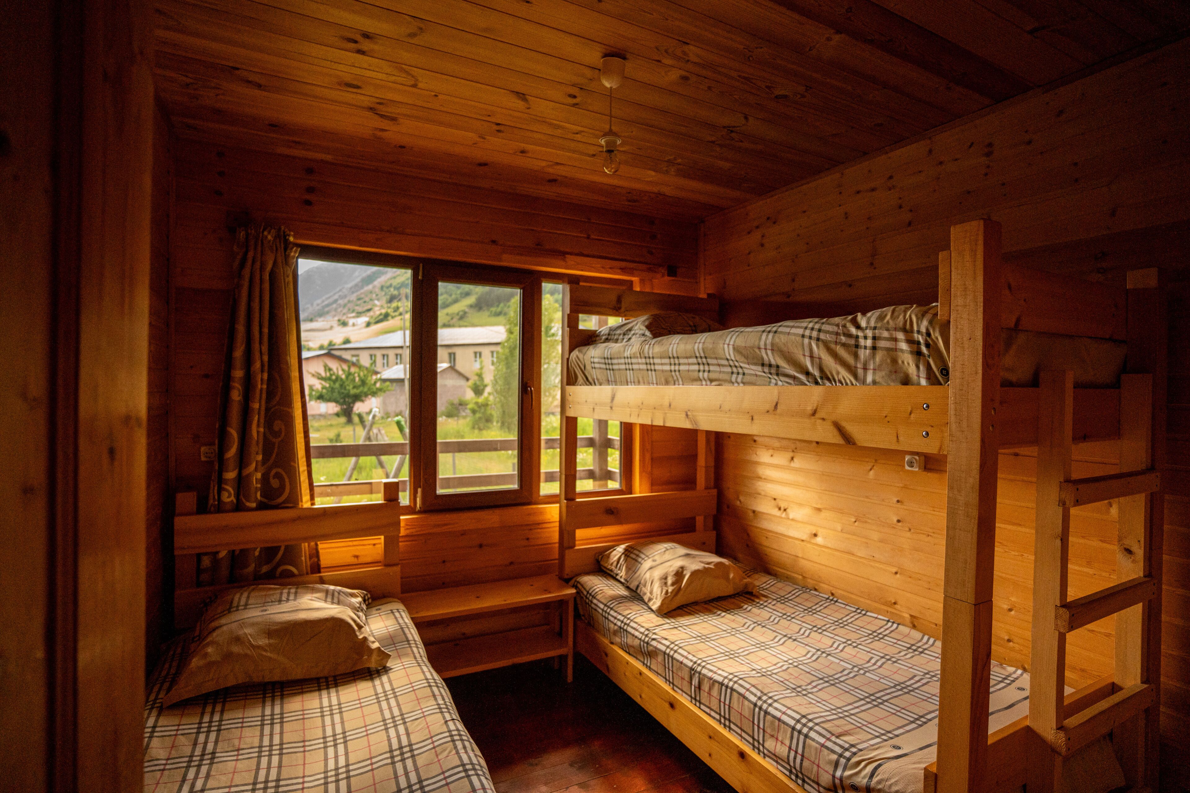 Uma cabana com duas beliches, uma janela com cortinas e vista para uma montanha.