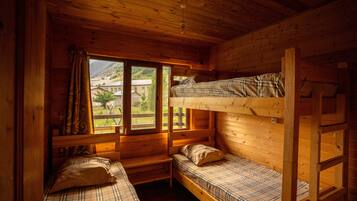 Una cabaña con dos literas, una ventana con cortinas y vistas a la montaña.