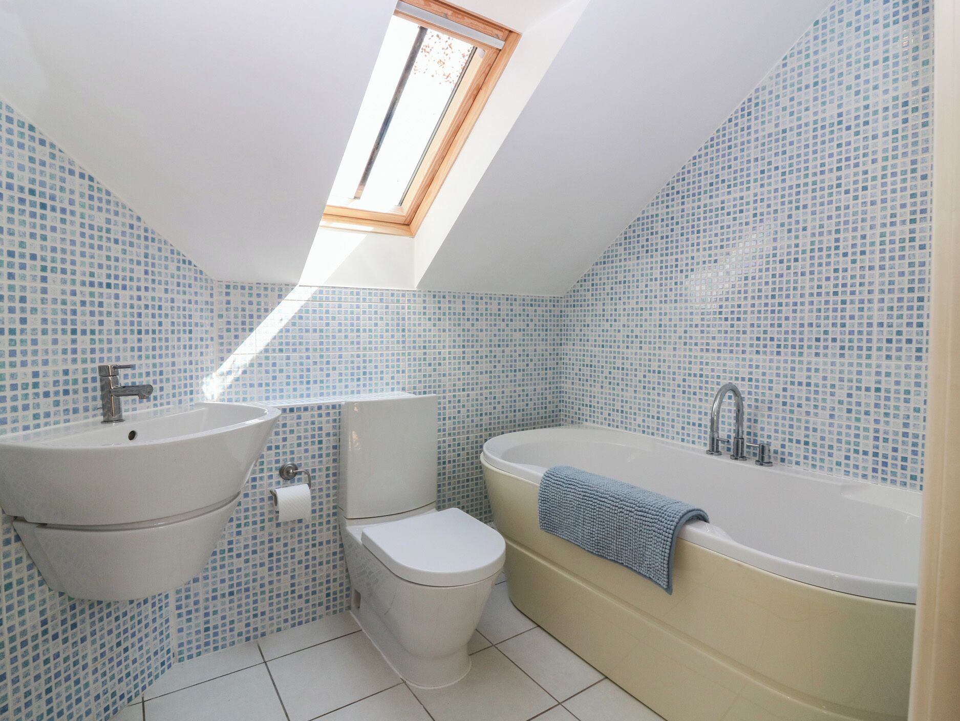 A bathroom with a skylight, a sink, toilet, and bathtub.