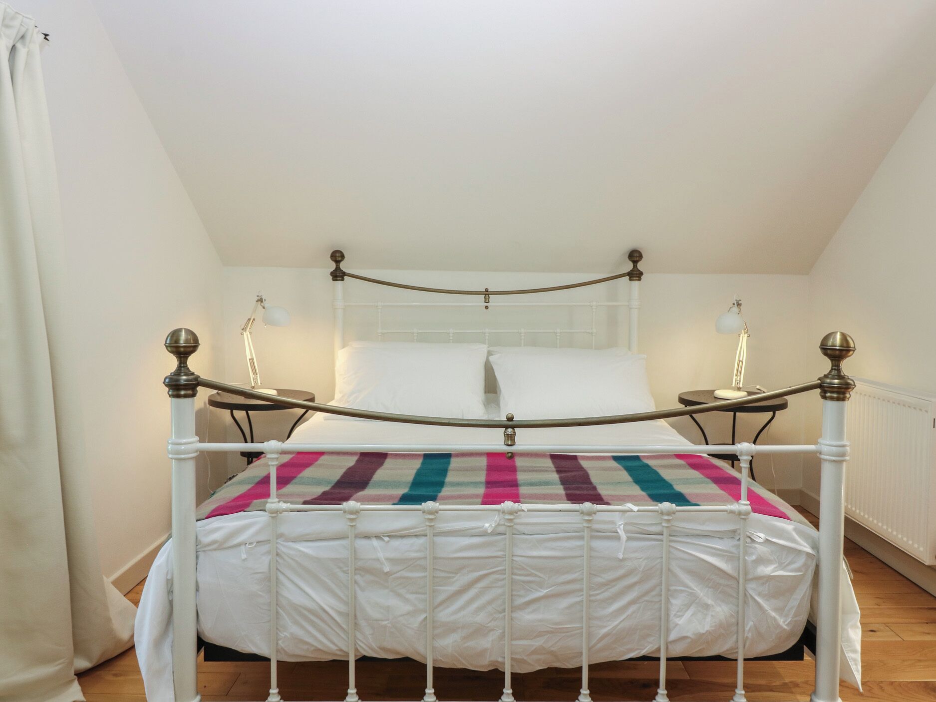 A white four-poster bed with a colorful striped bedspread, two bedside lamps, and a white headboard.