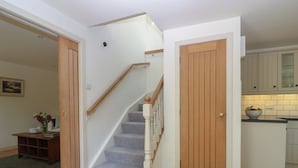 Una escalera que lleva al segundo piso, una puerta de madera y una zona de cocina con armarios.