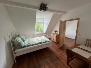 Ein Schlafzimmer mit schrägem Dach, einem Bett, einer Kommode, einem Fenster und einer Tür.