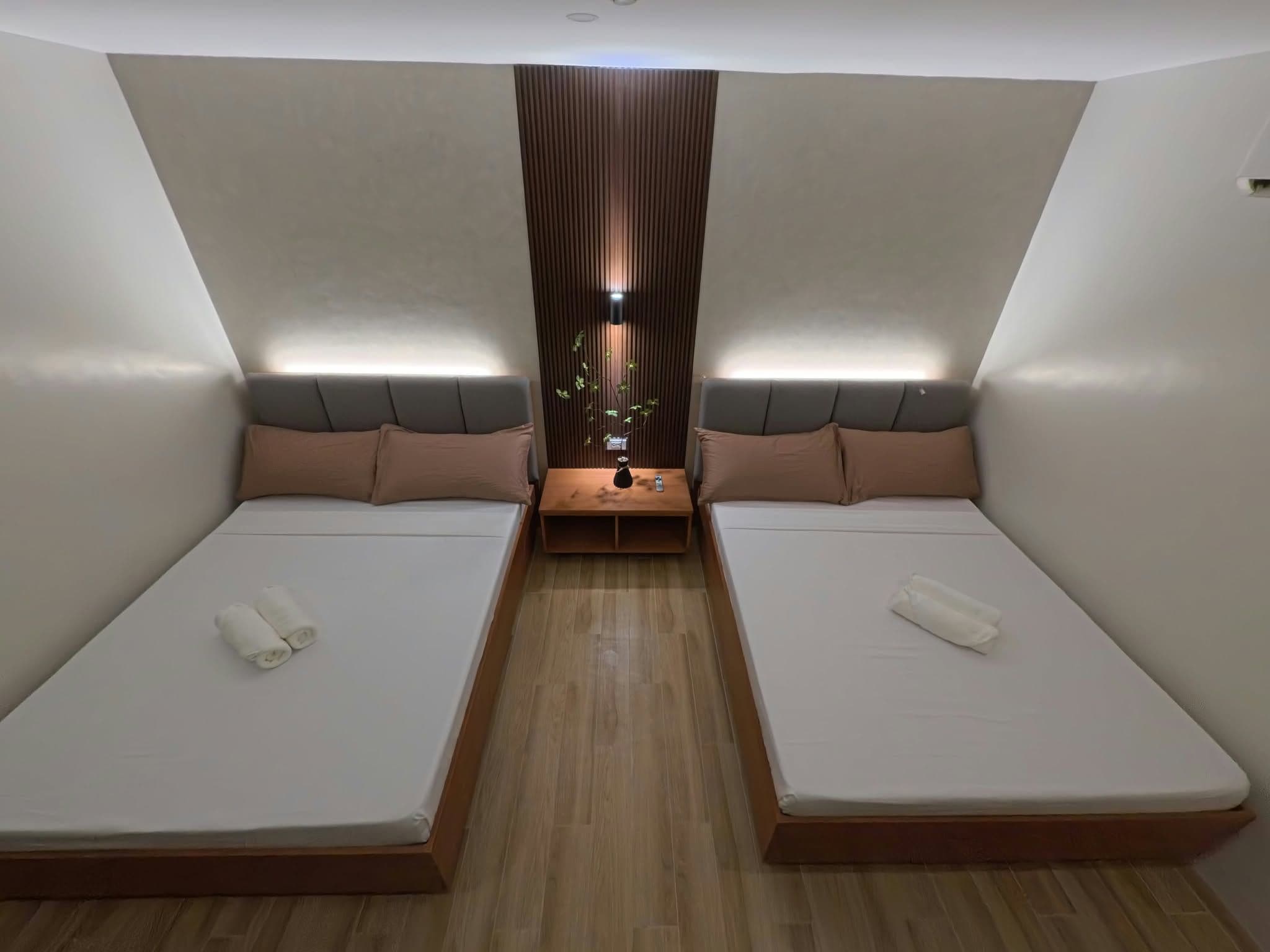A compact room with two beds, a small table, and a decorative plant.