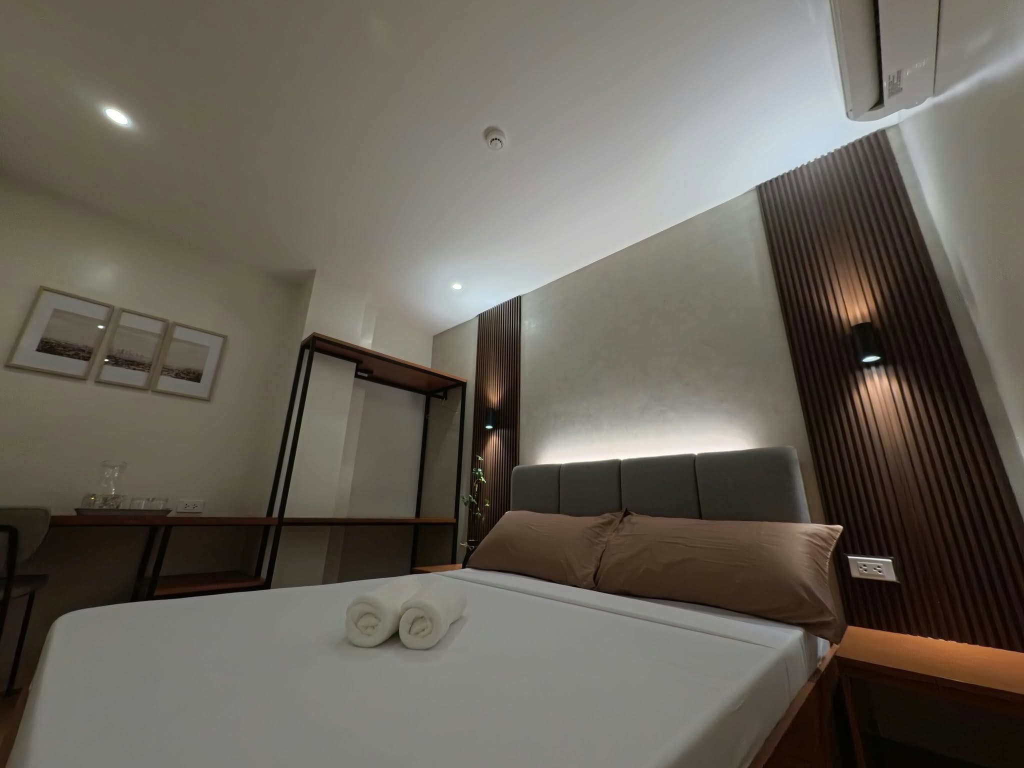 A hotel room with a bed, bedside table, and a wall-mounted air conditioner.