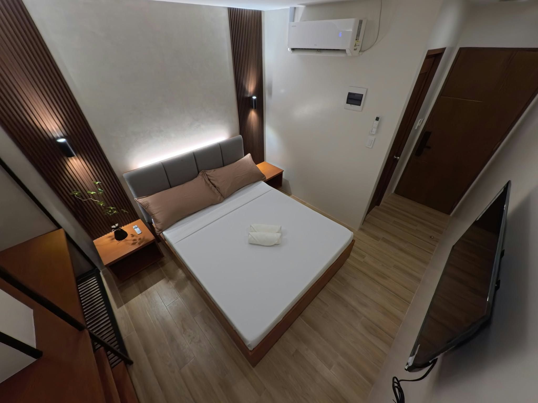 Habitación de hotel moderna con cama, mesita de noche y televisor montado en la pared.