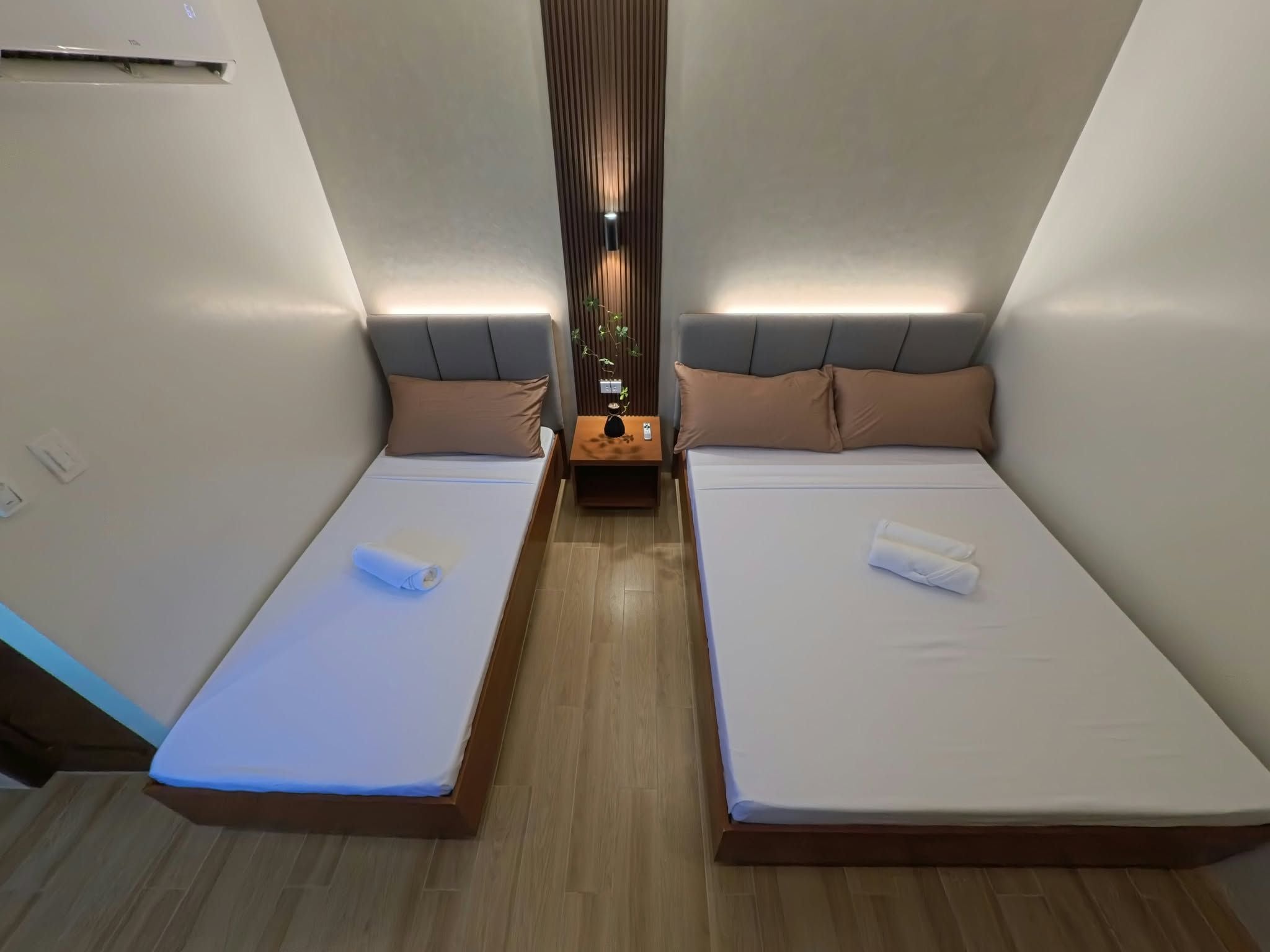 Une chambre de taille modeste, équipée de deux lits, d’une table de chevet centrale et d’un luminaire vertical.
