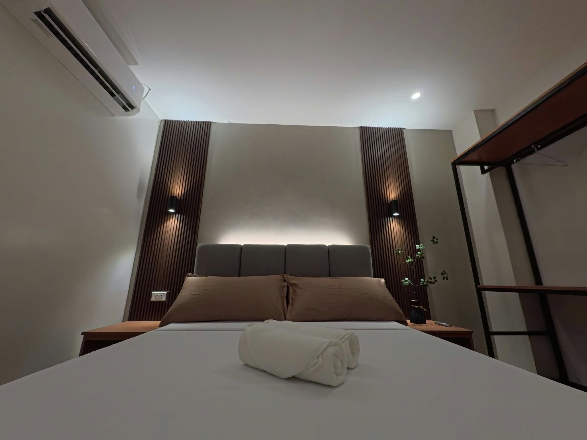 A modern bedroom with a large bed, a headboard with built-in lighting, and a wall-mounted air conditioner.