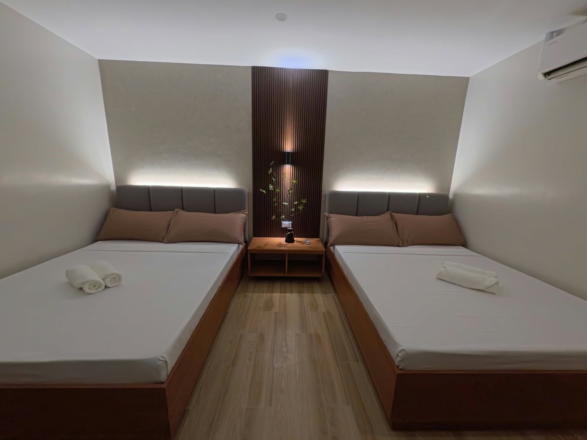 Una habitación de hotel moderna con dos camas, una mesita de noche central y un panel de madera vertical.