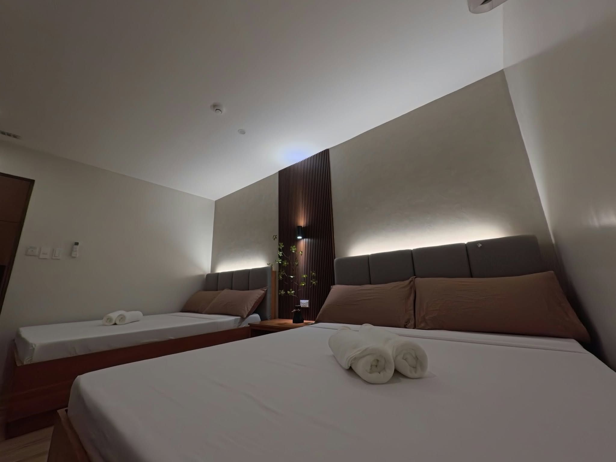 A hotel room with two beds, a wooden headboard, and a wall-mounted light fixture.