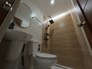 A bathroom with a toilet, sink, mirror, shower, and tiled walls.