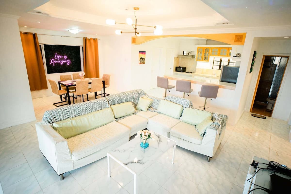 Una sala de estar moderna con un sofá seccional, una mesa de comedor y una cocina visible a través de un arco.