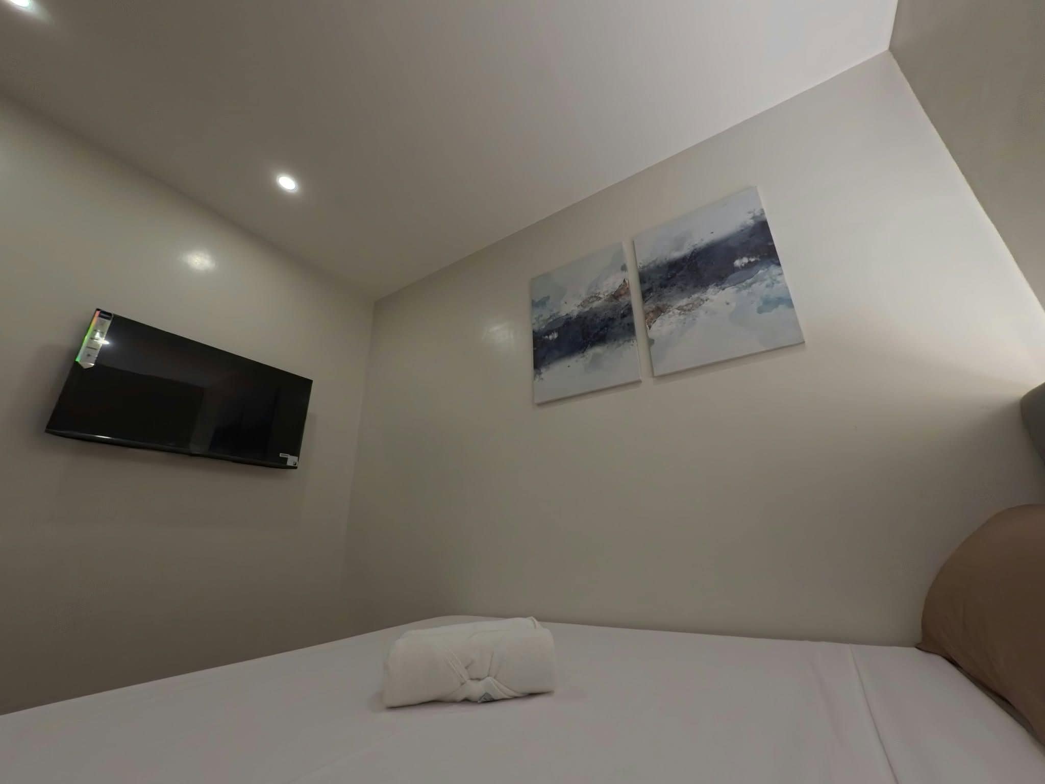 A hotel room with a bed, a flat-screen TV mounted on the wall, and two abstract paintings.