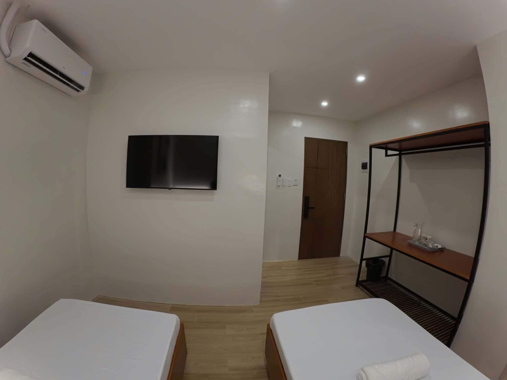 A hotel room with two beds, a TV mounted on the wall, and a wooden floor.