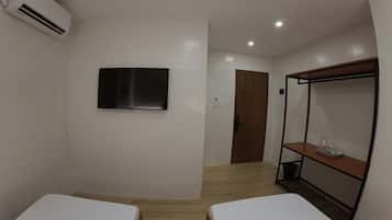 A hotel room with two beds, a TV mounted on the wall, and a wooden floor.