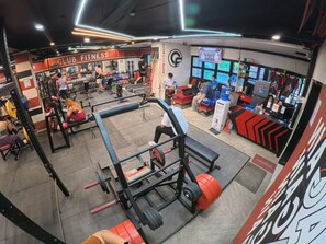 Un gimnasio con diversos equipos de ejercicio, una zona de pesas y un área de descanso con una pantalla de televisión.