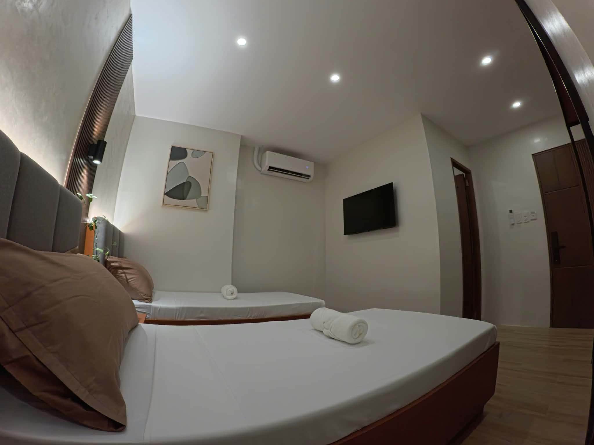 A modern hotel room with two beds, a flat-screen TV, an air conditioning unit, and a wall-mounted artwork.