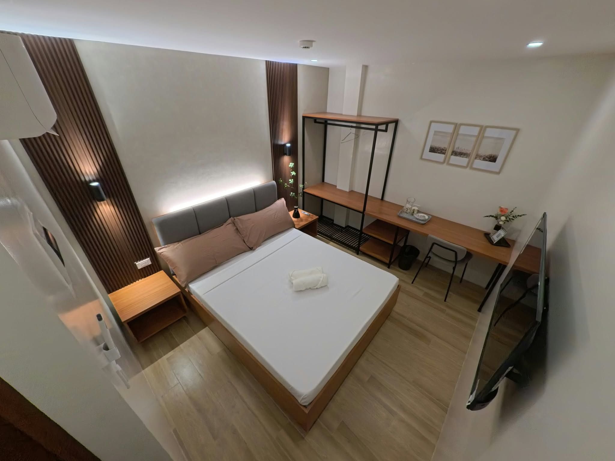 A modern hotel room with a bed, bedside table, desk, and a TV.