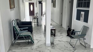 A spacious hallway with a marble floor, multiple seating areas with chairs, and a door leading to another room.