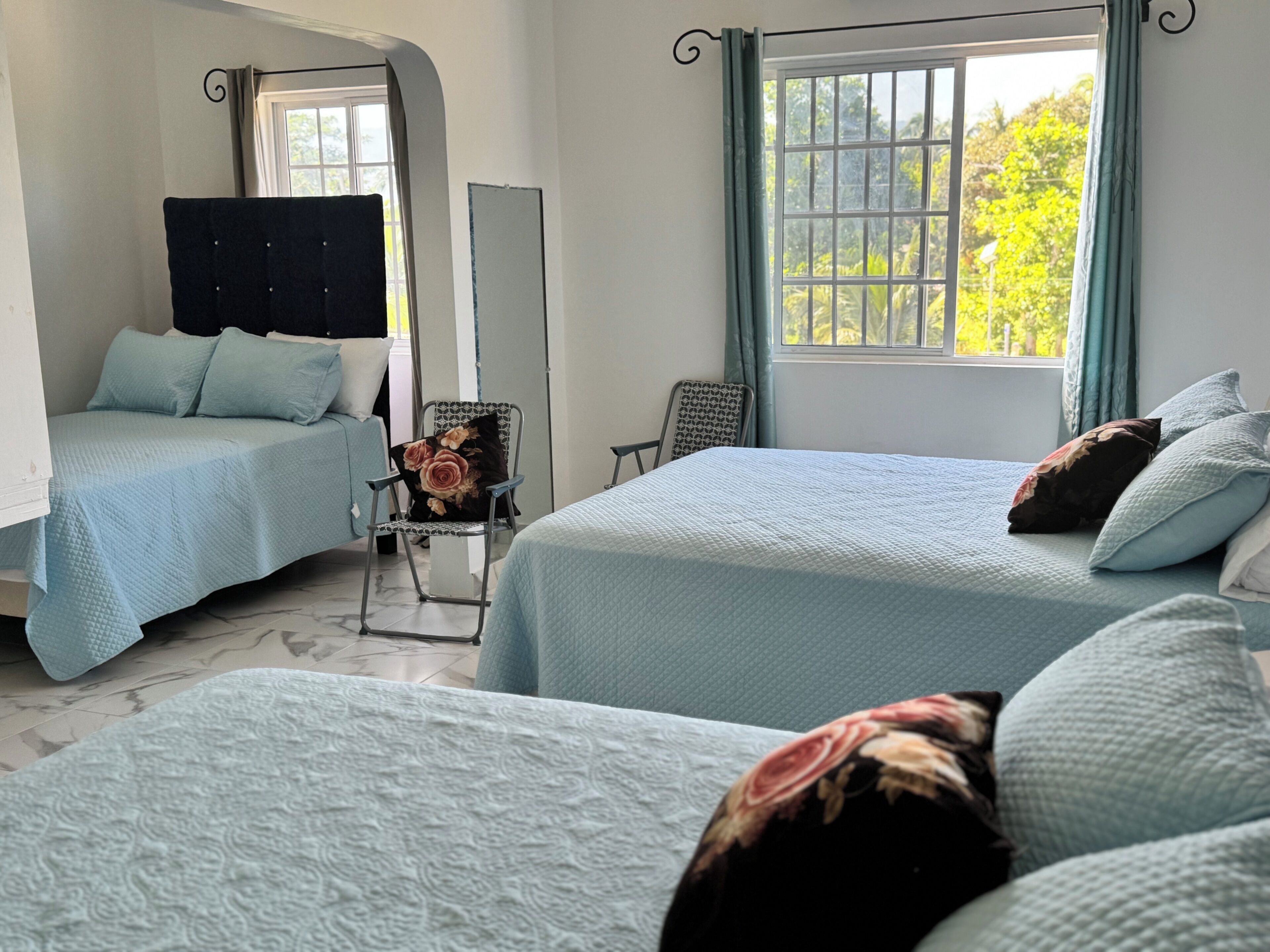 Una habitación con dos camas, una silla y un ventanal con cortinas.