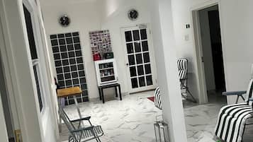 A spacious room with a marble floor, a dining table, chairs, a small table with a vase, and a clock on the wall.